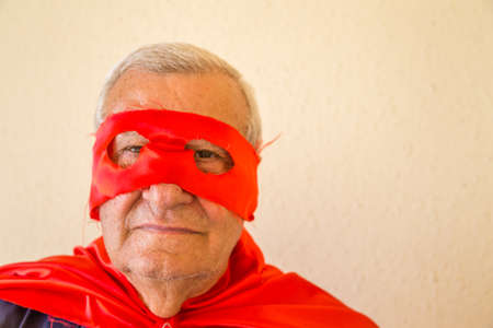 close-up of senior citizen wearing superhero costume with red cape and mask with happy but tough eyesの写真素材