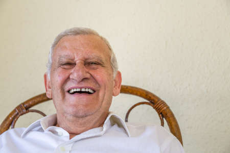 Happy elderly man laughing while sitting against a yellow wall, concept of joyの写真素材