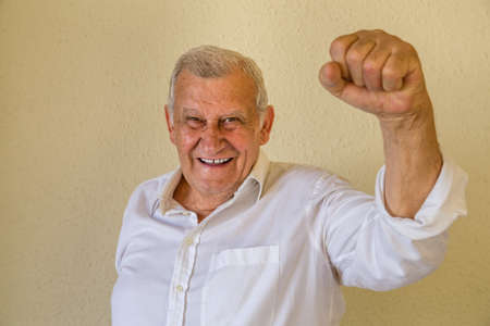 Happy pensioner man standing with fist clenched in victoryの写真素材