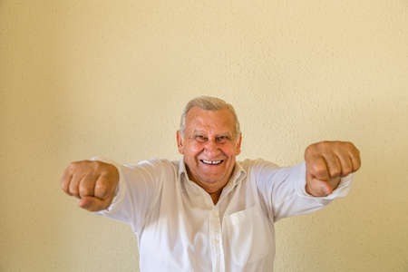 Happy confident old man with hands out posing as a superhero isolated on yellow wall backgroundの写真素材