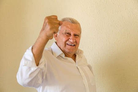 Happy successful senior man, winning pensioner pumping fist and celebrating victory isolated on yellow wall backgroundの写真素材