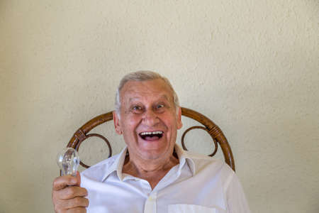 Excited elderly man isolated on yellow wall background  holding bulb meaning idea and innovation conceptの写真素材