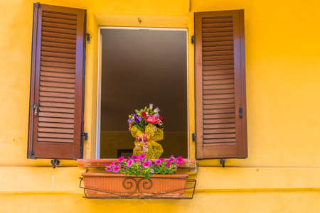 Violet petunia hanging from the window sills of an ancient house in medieval village in italy, country of old times and colorful flowersの写真素材