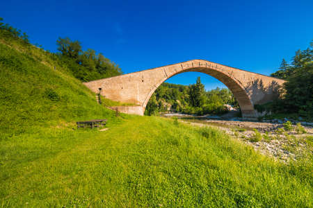 green grass to ancient XVI bridge with donkey back structure, one of wonders of Italyの写真素材