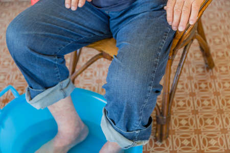 Legs and feet of old man having foot-bath in water basinの写真素材