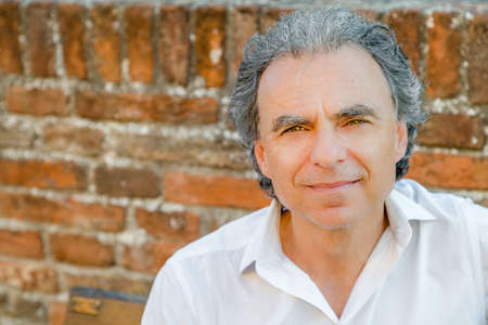 mature man with soft skin smiling against old brick wall backgroundの写真素材