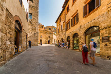 tourists shopping in street with typical stone buildings of the medieval village of San Gimignano near Siena under the sun of Tuscanyの写真素材