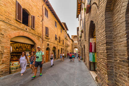 tourists shopping in street with typical stone buildings of the medieval village of San Gimignano near Siena under the sun of Tuscanyのeditorial素材