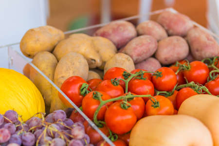 red tomatoes, yellow and red potatoes, black grapes, yellow melons in transparent boxesの写真素材