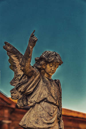 statue of young angel looking down and raising finger up to the skyの写真素材