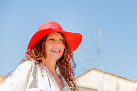 Low angle outdoor portrait of a beautiful fashionable woman wearing a red wide sunhat against a blue skyの写真素材