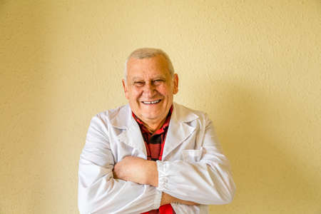 senior country doctor with white medical gown and checkered shirt smiling and crossing armsの写真素材