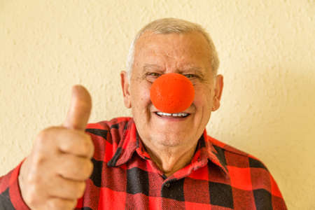 elderly smiling and wearing checkered shirt and red nose while raising thumb upの写真素材