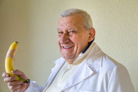 Old country doctor smiling while holding a large  bananaの写真素材