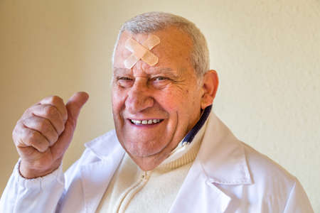 old doctor with patches on the forehead smiling and showing thumbs upの写真素材