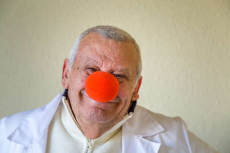 Old country doctor with clown red nose smilingの写真素材