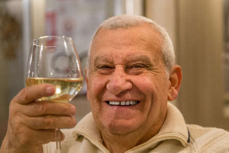 happy old man smiling and drinking white wine in a restaurantの写真素材