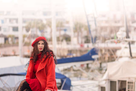 mature woman with vintage red hat and dress smiling with light flare on her top right, with boats of...