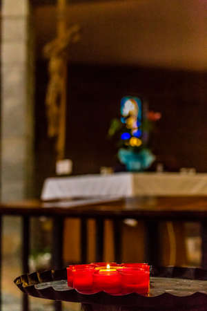 one white candle burning amongst extinguished red ones with Crucifix and stained glass in the backgroundの写真素材