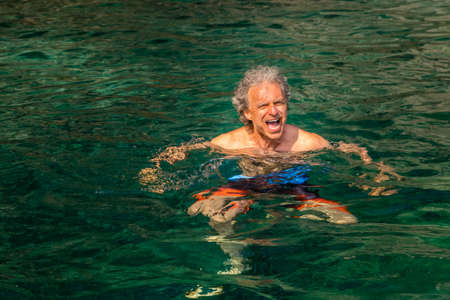 mature man having fun while swimming in a emerald green sea