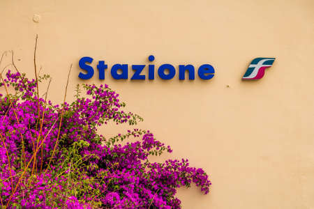 CORNIGLIA (SP), ITALY - JUNE 17, 2018: bush of bougainvillea glabra is covering the wall of a railway station with logo of Italia railway companyのeditorial素材