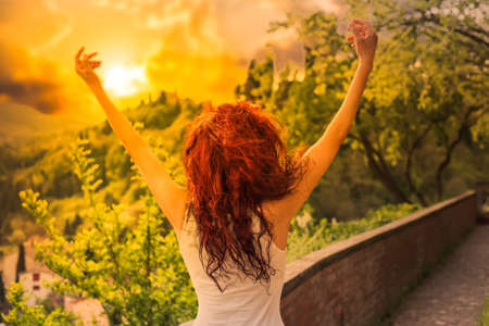 young girl greeting sun and gleefully spreading arms while facing sunの写真素材