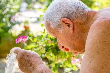 Senior man watering flowers with a rubber tubeの写真素材
