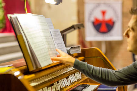 FORLI, ITALY - OCTOBER 26, 2018: Organist prepares the scores with the Templar cross in the background. Catholic Templar Knights participate in the ritual of Holy Massのeditorial素材