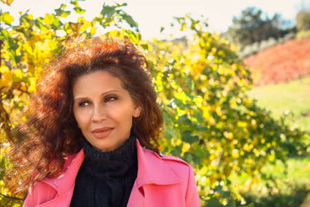 Mature woman with sun tanned skin wearing coral dust coat enjoys the panorama of the cultivated...