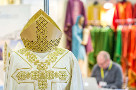 BOLOGNA, ITALY - FEBRUARY 18, 2019: Sacred vestments with in background booth presenter working on laptop while waiting for visitors at stand of MARANATHA in DEVOTIO Exhibitionのeditorial素材
