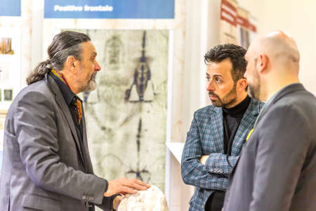 BOLOGNA, ITALY - FEBRUARY 18, 2019: booth presenter talking with visitors at stand of Turin Shroud...