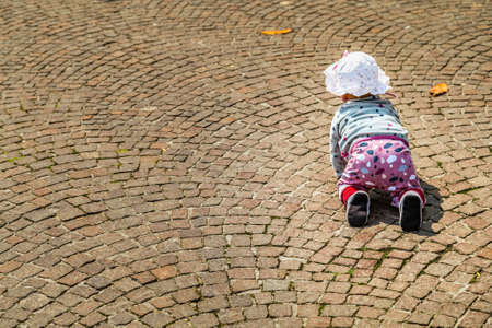 back of cute funny baby wearing white hat and pink pants crawling on cobbledstones on Italyの写真素材