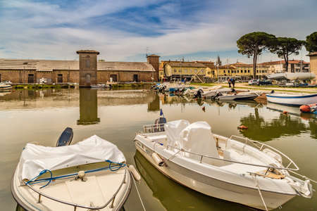 CERVIA (RA), ITALY - MAY 17, 2019: boats mooring in port channel of Cervia with medieval tower in...