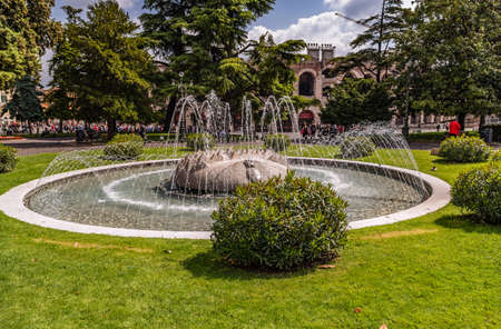 VERONA (VR), ITALY - MAY 10, 2019: water flowing from fountain and  tourists walking in Piazza Bra in historical center of Verona, Italian romantic townのeditorial素材