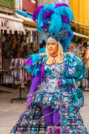 BURANO (VE), ITALY - FEBRUARY 21, 2020: masked woman walking in the typical street of Burano, ancient fishing village during Carnivalのeditorial素材
