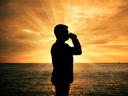 Silhouette man drinking coffee at sunsetの写真素材