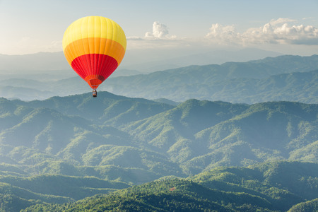 Colorful hot air balloon above forest mountainの写真素材