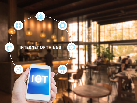 Hand holding mobile phone with Internet of things on screen with blurred coffee shop backgroundの写真素材