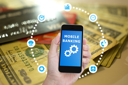 Hand holding mobile phone with Mobile banking application on blurred image of US. banknote and credit card backgroundの写真素材