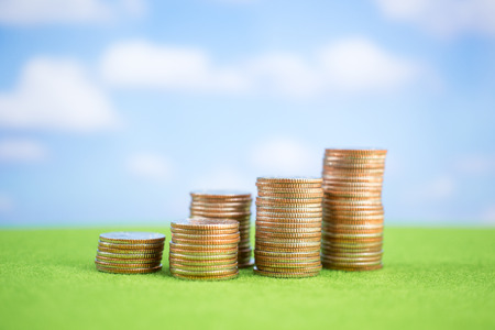 Stack of coins on green and blue sky backgroundの写真素材