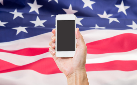 Man hand holding mobile phone with United State of America flag backgroundの写真素材