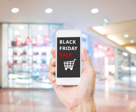 Hands holding mobile phone with Black Friday sale on screen on blurred image of shopping mallの写真素材