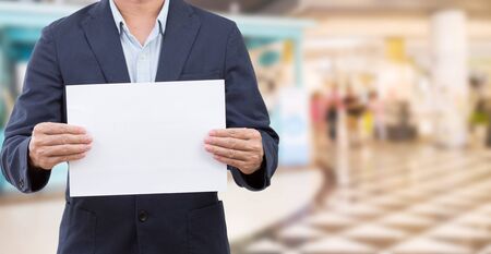 Man holding blank white board on blur shopping mall backgroundの写真素材