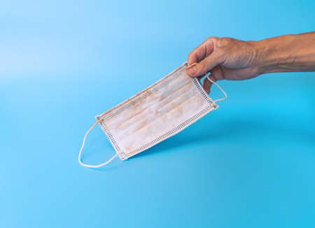 Man hand holding used face mask on blue background