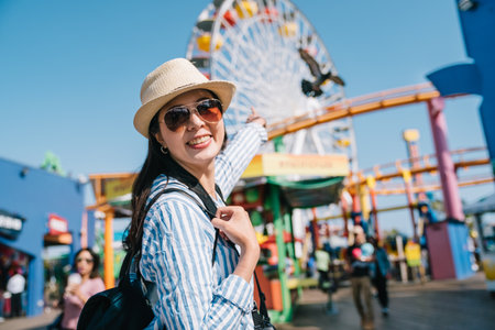 Portrait of young asian tourist woman in hat and sunglasses on amusement park background