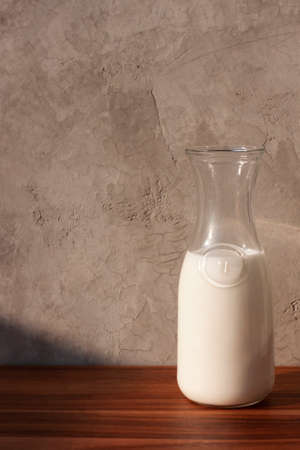 Milk in a glass jug on a wooden table against a concrete wallの写真素材
