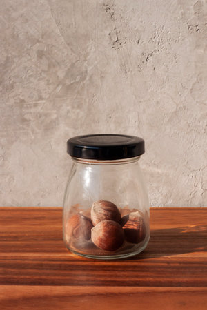 A jar of hazelnuts on a wooden table against a gray wall.