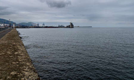 northern industrial fishing village with sailboat in calm sea and cloudy spring skyの写真素材