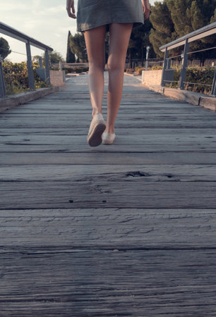 Blonde-haired woman strolling relaxed on wooden bridge de-stressing from city lifeの写真素材