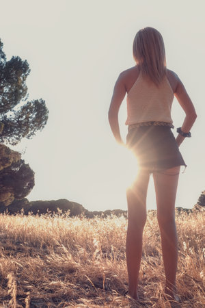 blonde-haired woman strolling through wheat field in shorts at sunsetの写真素材
